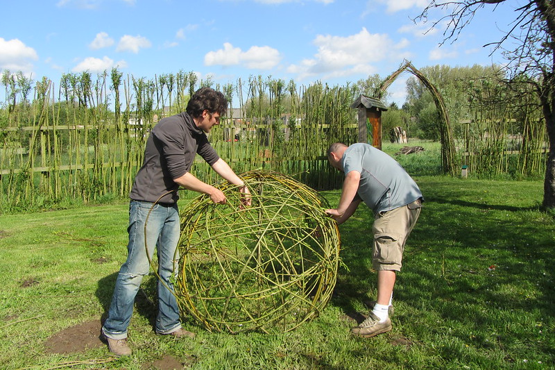 deux hommes en train de tisser une boule en osier sur une cadre en métal